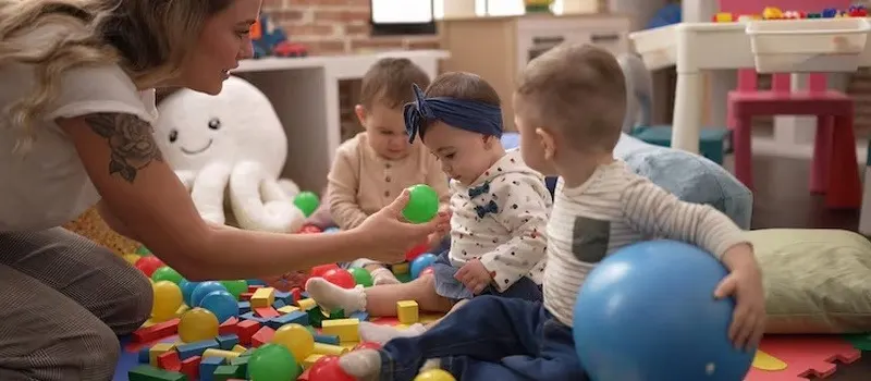 How To Start A Daycare | Preschool Business Guide 2026 1 Teacher And Preschool Students Are Playing With The Ball On The Floor
