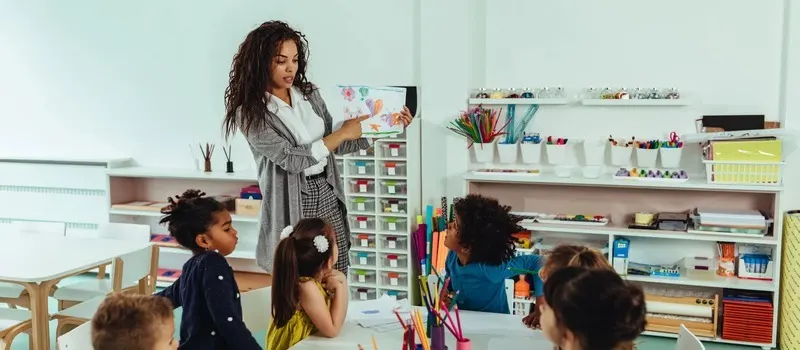 Teacher-To-Child Ratio Guide And How It Shapes Classroom Design 1 Image Of A Caregiver Showing A Drawing Book Of A Child To A Group