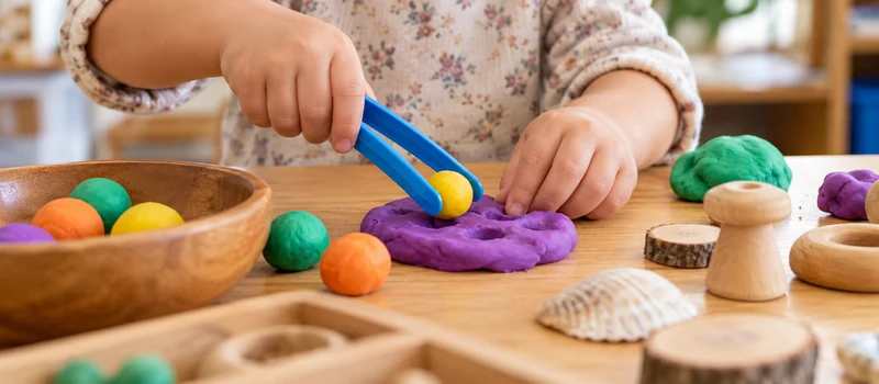 How Can Preschool Classrooms Build Handwriting Motor Skills? 1 Preschool Child Building Hand Strength With Playdough And Tongs